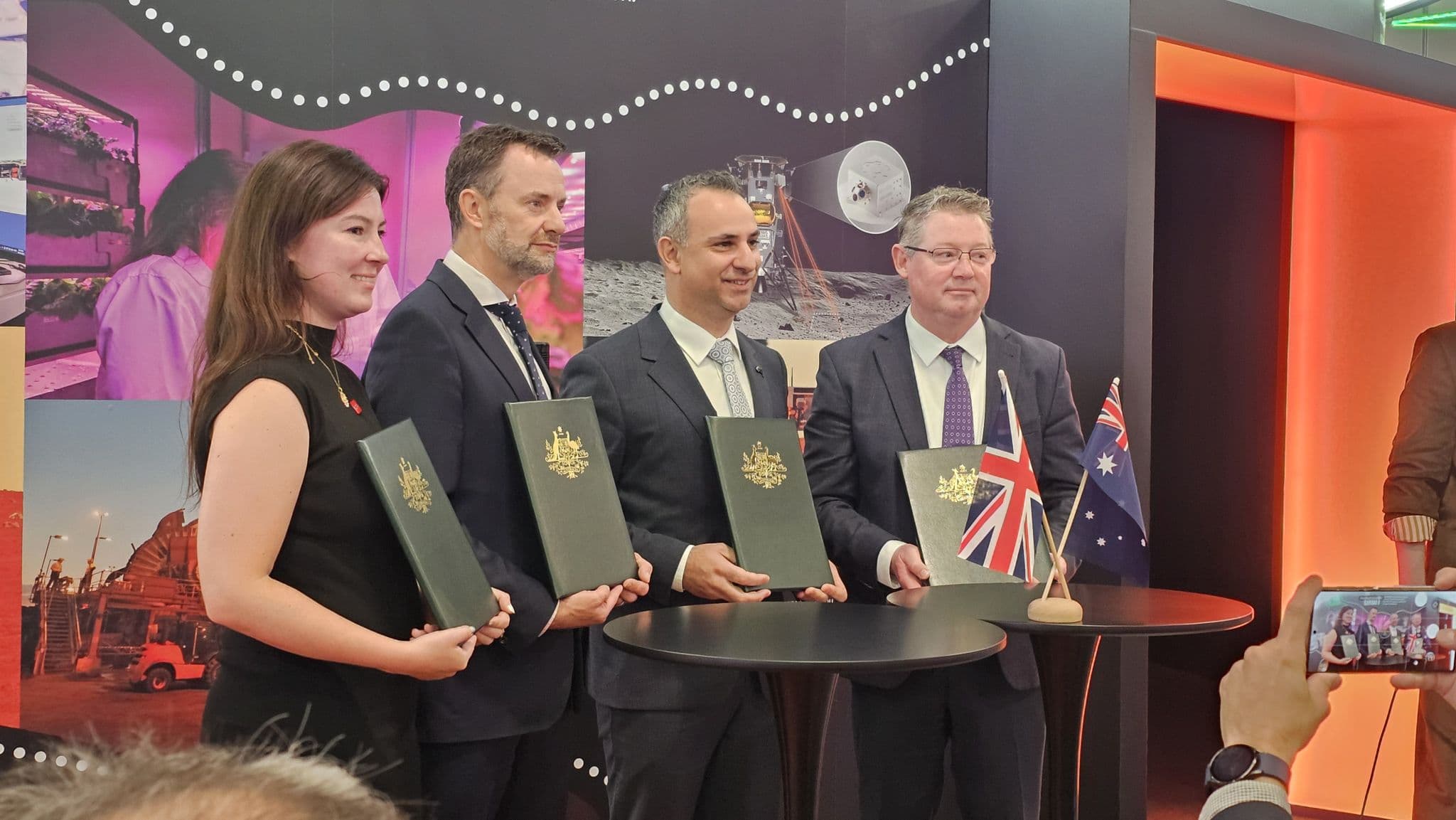 UK and Australian representatives holding signed agreement folders at the UK Space Bridge signing ceremony, with UK and Australian flags.